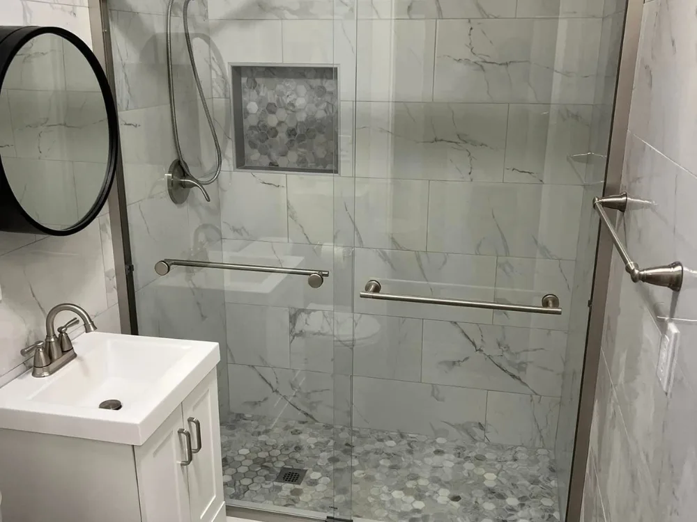 Bathroom renovation project with marble-look wall tile, glass shower doors, and custom niche with hexagon mosaic.